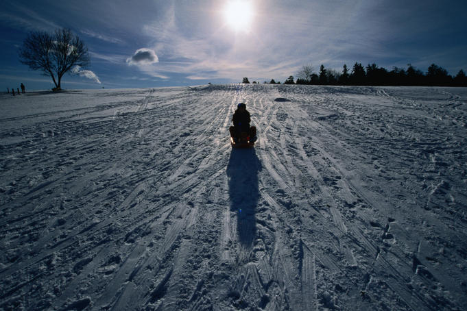 A woman on a sled on a snowy slope in the winter sun.