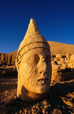 The earthquake damaged head of Heracles (or Hercules) at Nemrut Dagi (Mount Nemrut) with the burial mound of King Antiochu in the background.